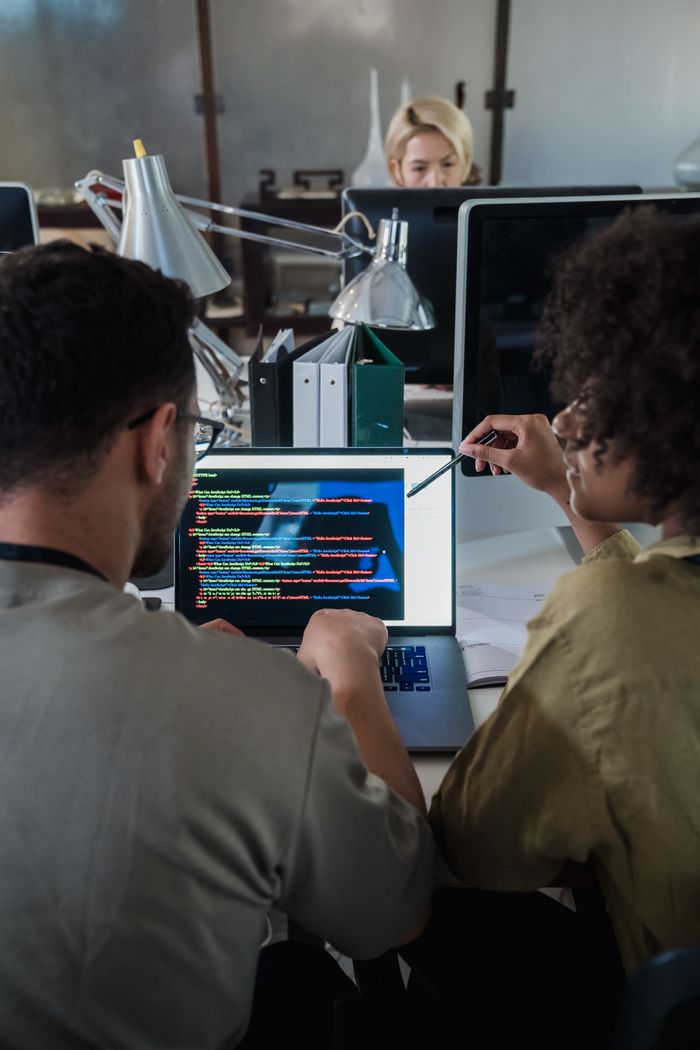 gallery-05 Two developers engage in software programming on a laptop in a modern office setting.