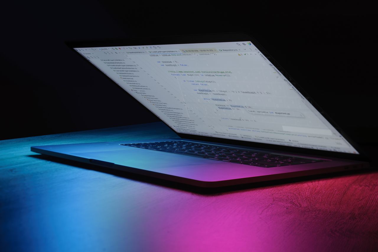 A partially open laptop displaying code, bathed in vibrant neon lighting.